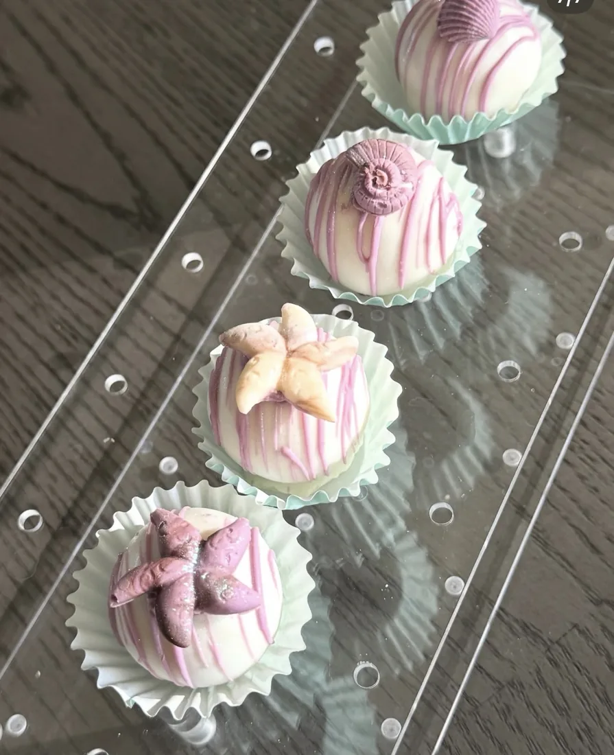 Pink and white drizzled cake bites in fluted liners topped with starfish and seashells