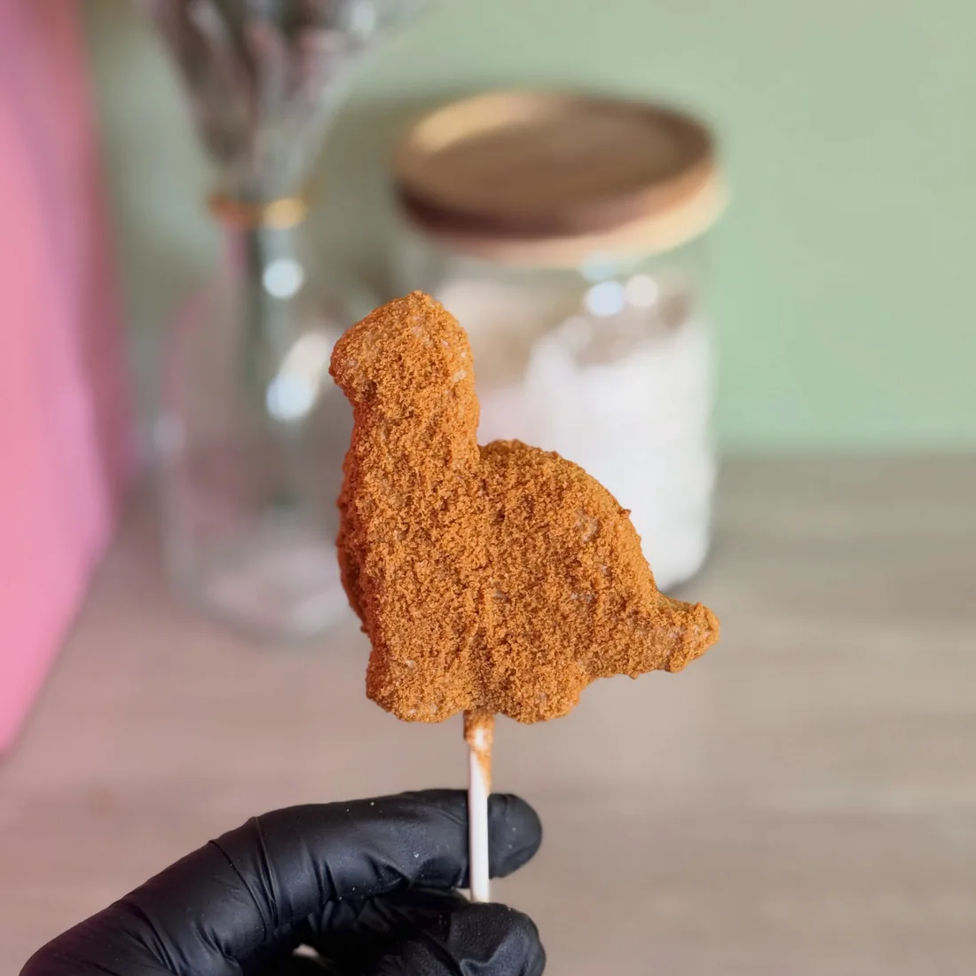 Gloved hand holding a single dinosaur nugget shaped cake pop