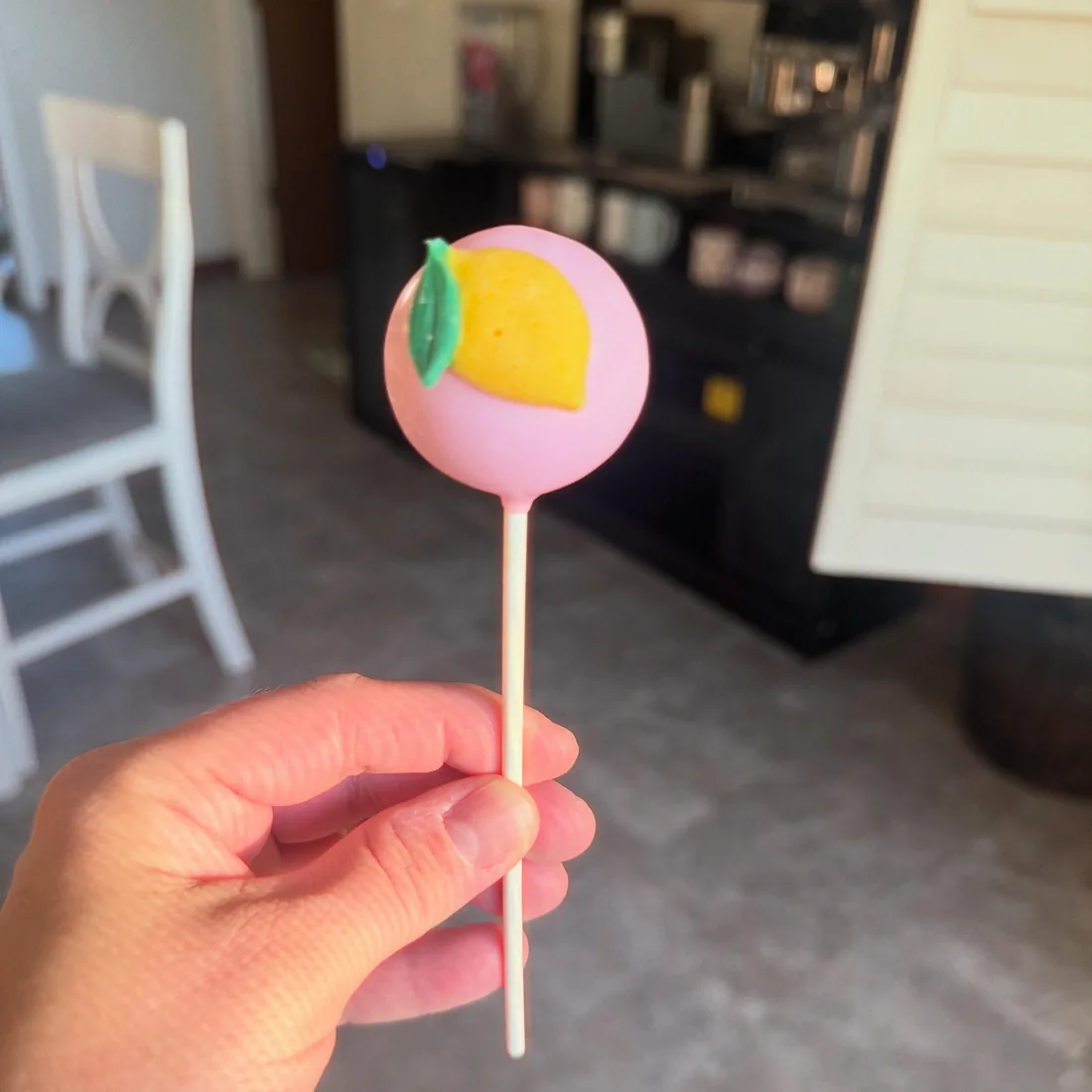 Hand holding a pink cake pop topped with a yellow fondant lemon