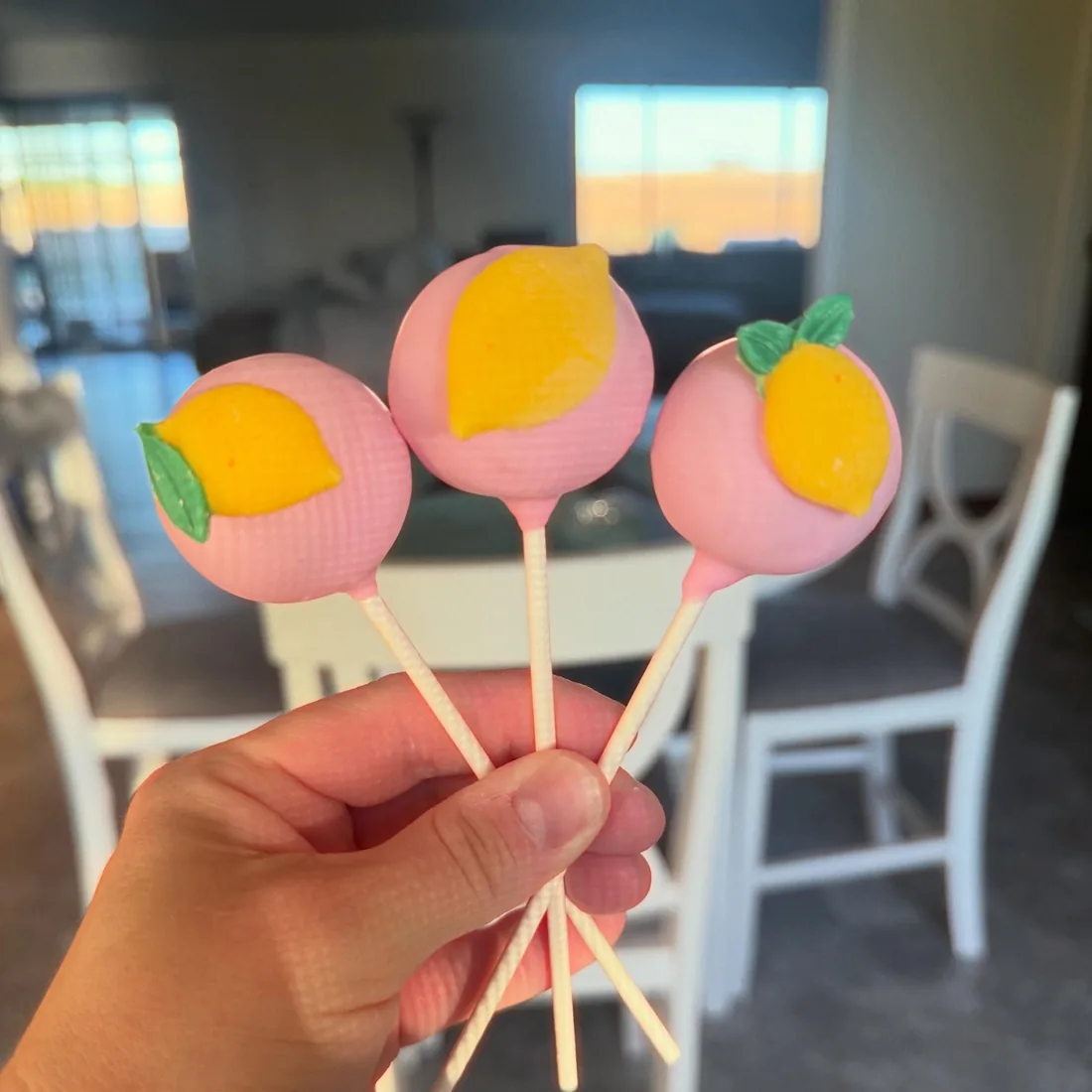 Three pink cake pops topped with fondant lemons and peaches
