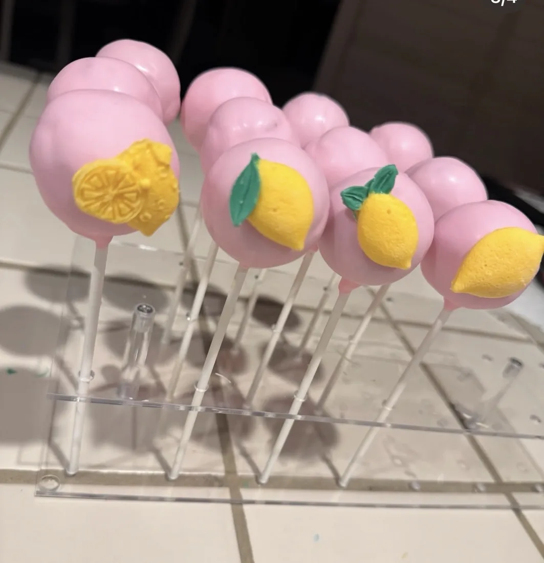 Pink cake pops topped with yellow fondant lemons on an acrylic stand