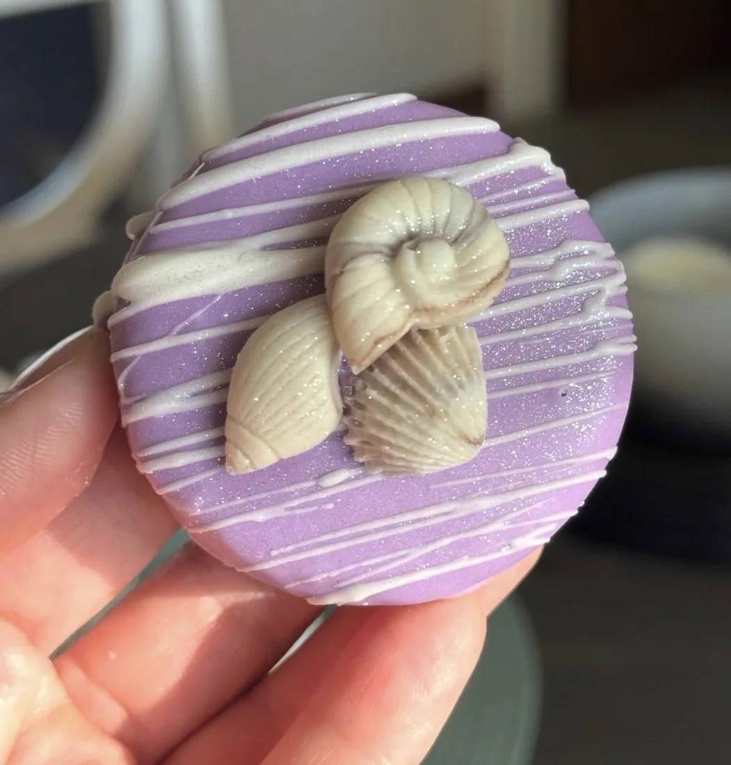 Hand holding a lavender dipped cake puck with a nautilus snail and shell topper