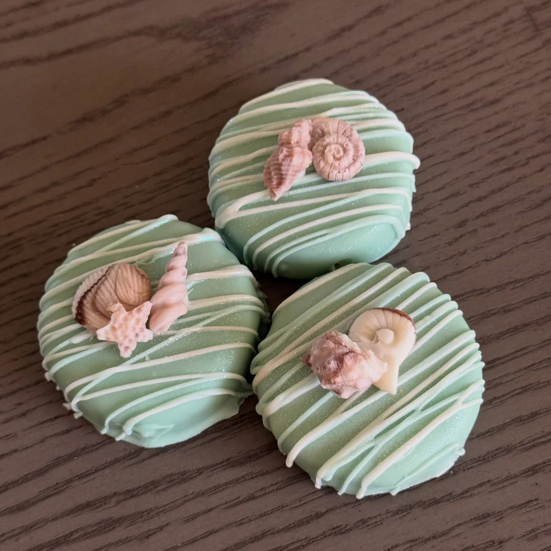 Three mint green dipped cake pucks topped with pink coral seashells