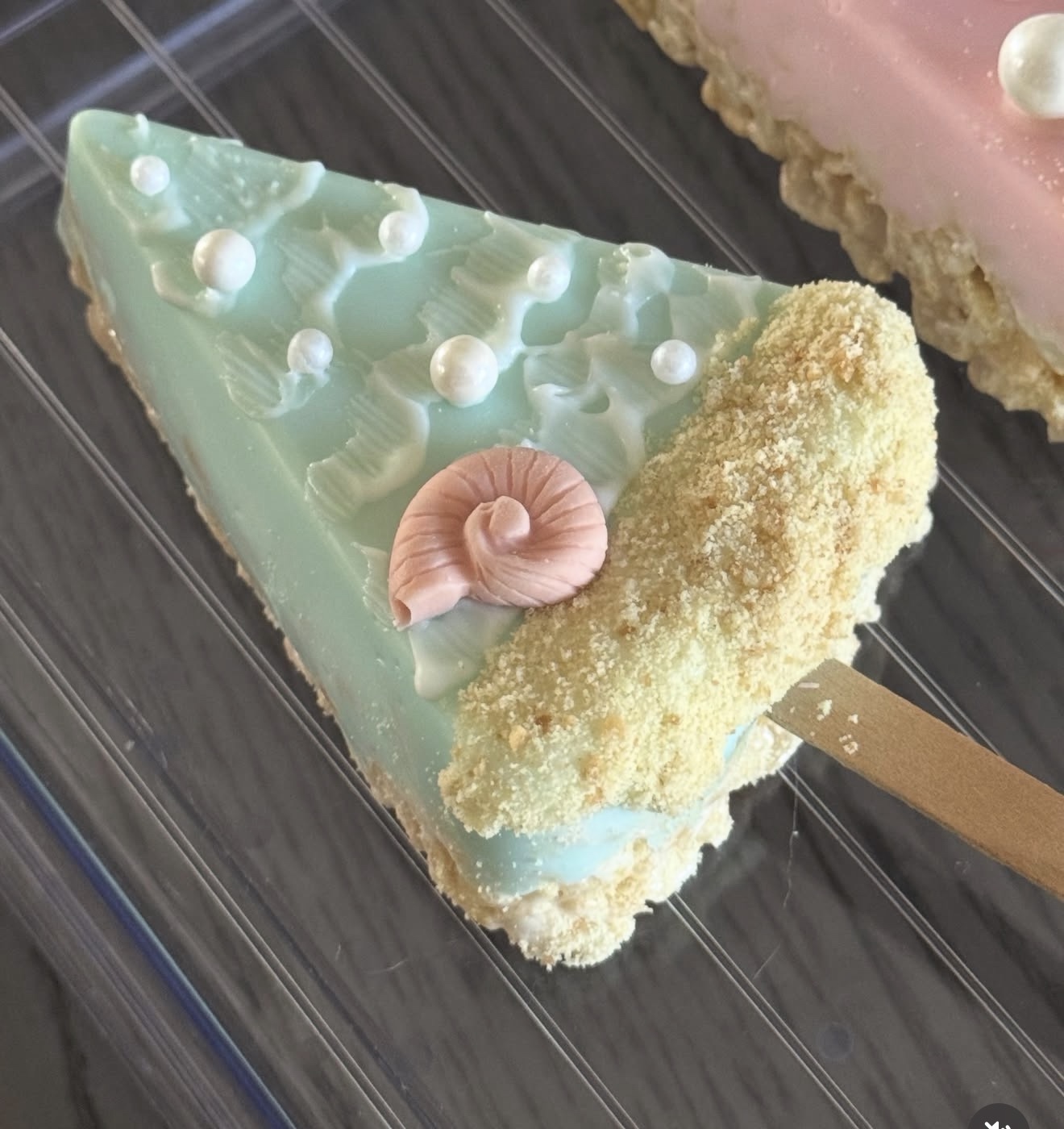 Close up of mint green rice crispy treat dipped in white chocolate with snail shell detail and pearl accents