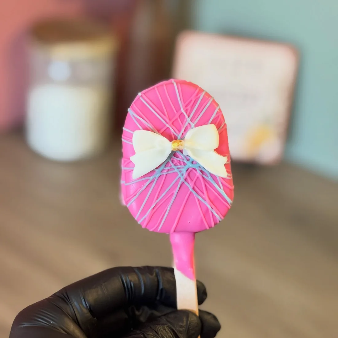 Hot pink cakesicle on a stick with white drizzle and a large white piped bow
