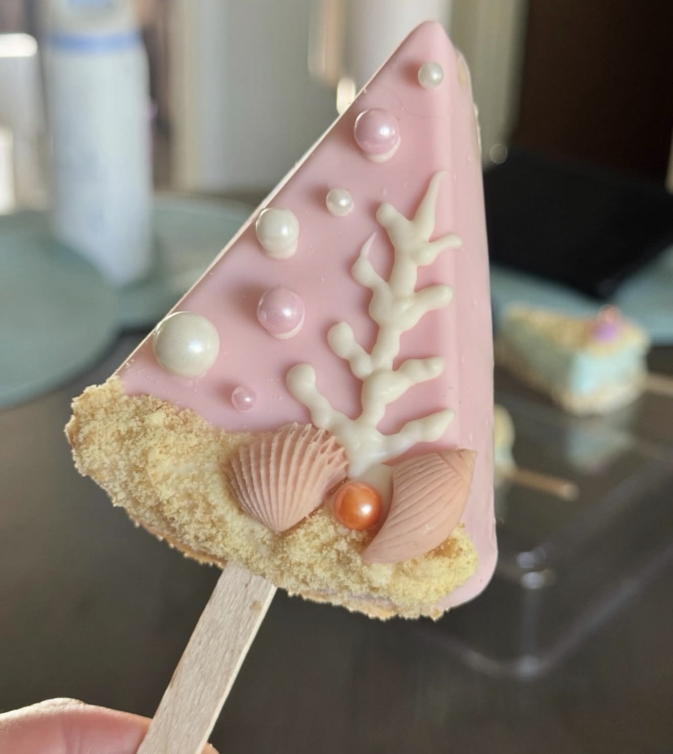 Pink rice crispy treat dipped in white chocolate with coral and shell decorations and pearl accents