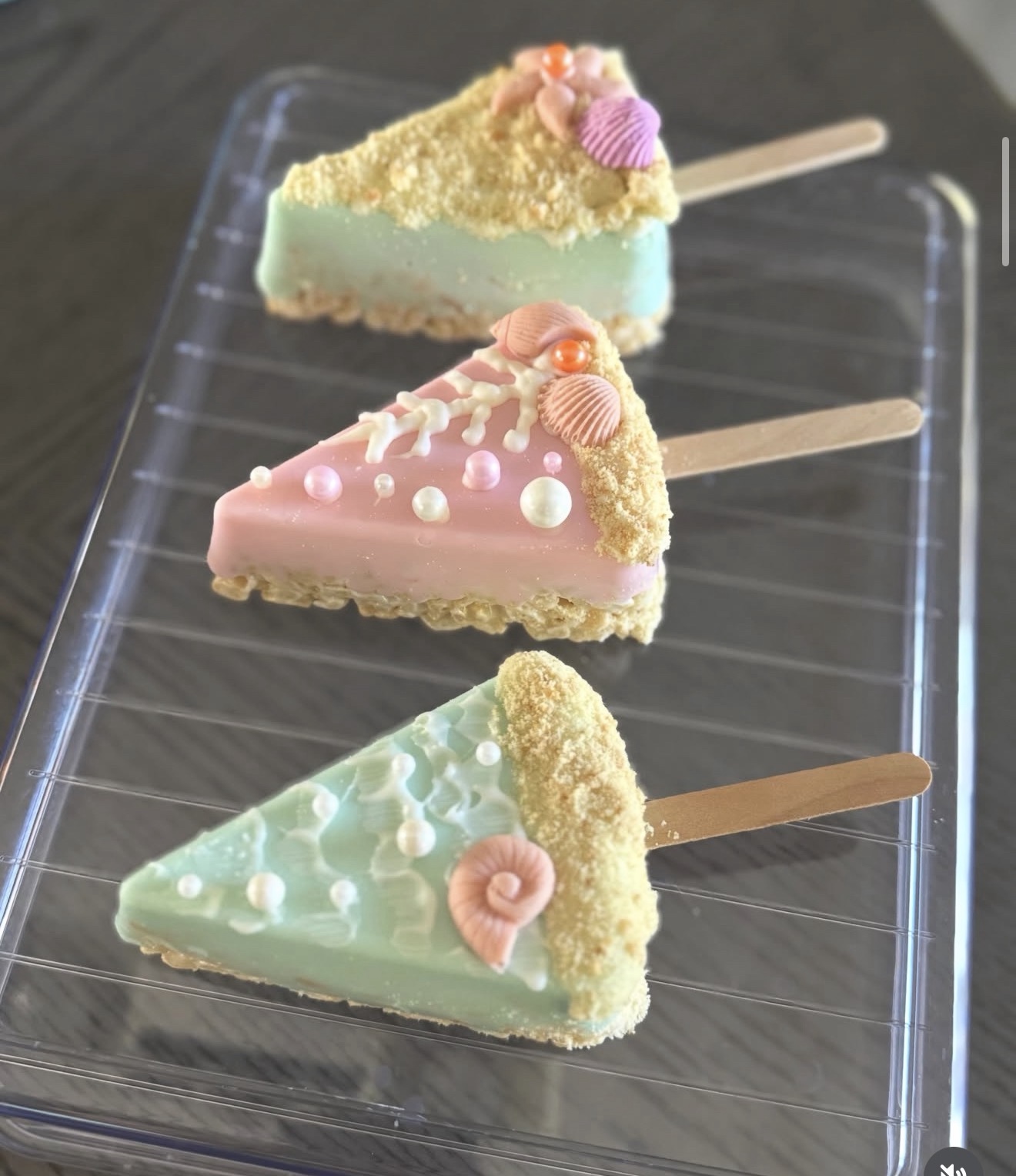 Beach themed rice crispy treats dipped in white chocolate, mint and pink with shell decorations on sticks