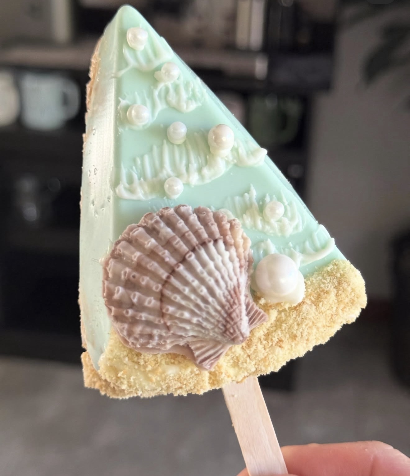 Mint green rice crispy treat dipped in white chocolate with large scallop shell and pearl accents