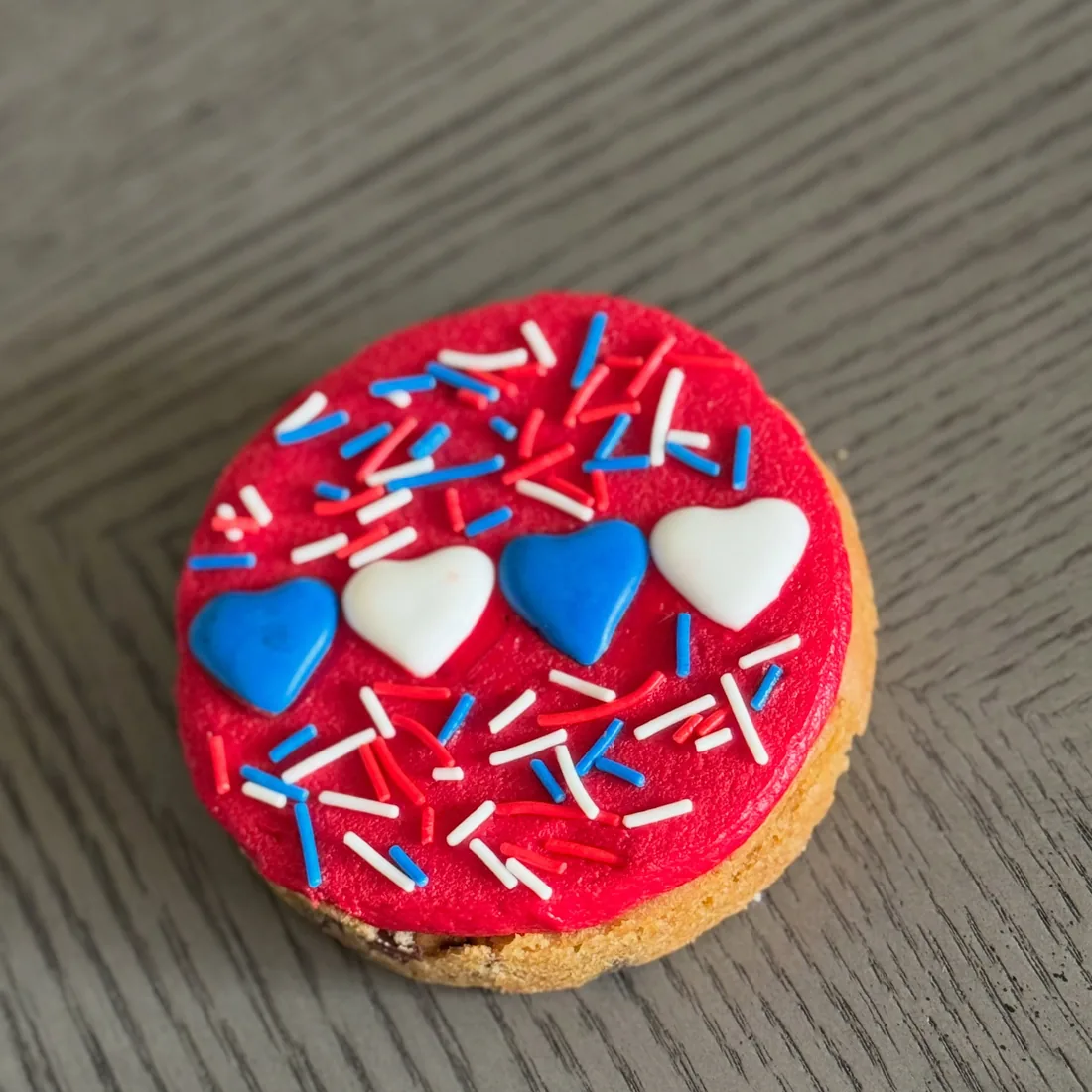 Red round cookie topped with white and blue fondant hearts and patriotic sprinkles