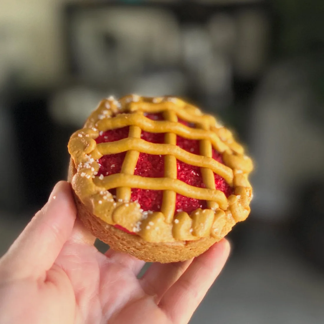 Hand holding a mini cherry cookie pie with a piped buttercream lattice