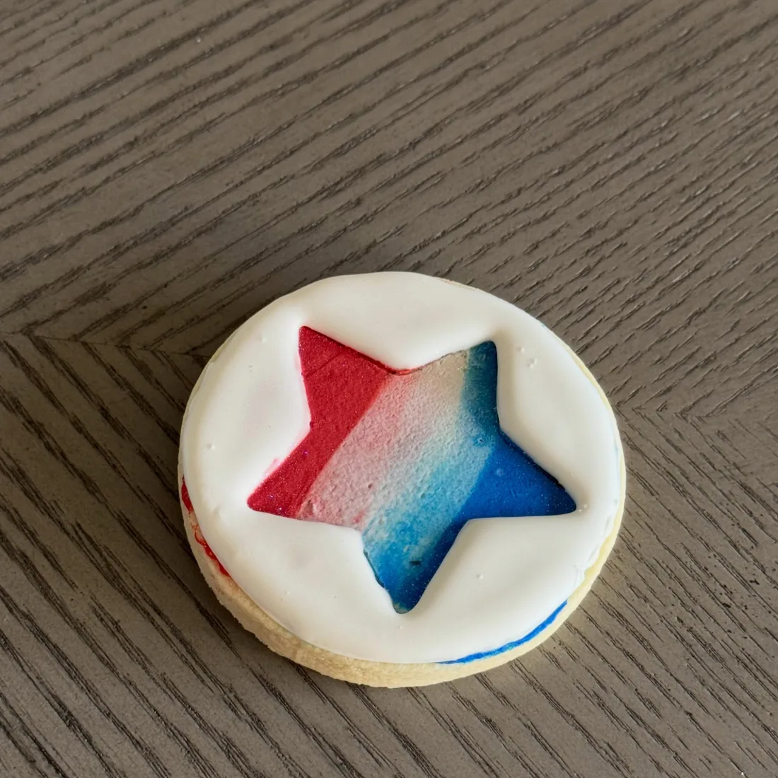 Round white cookie topped with a red and blue ombré fondant star