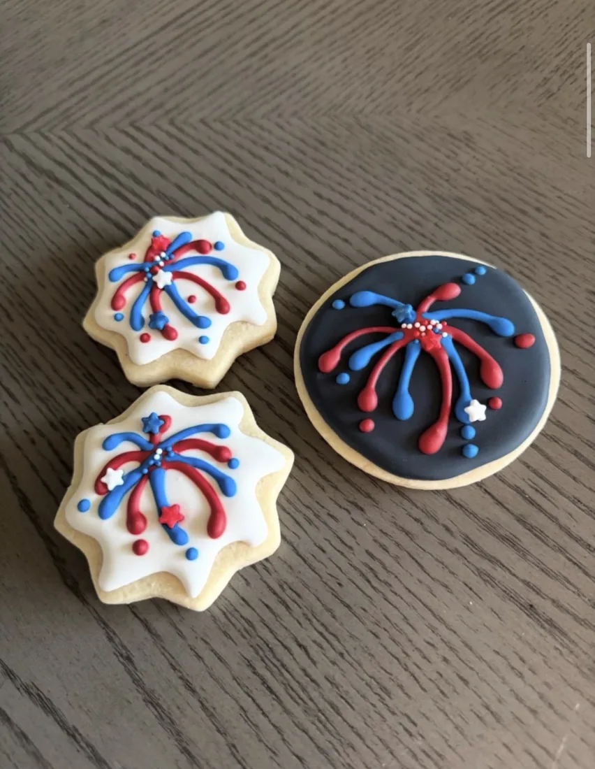 Two star cookies and a navy round cookie piped with red and blue fireworks