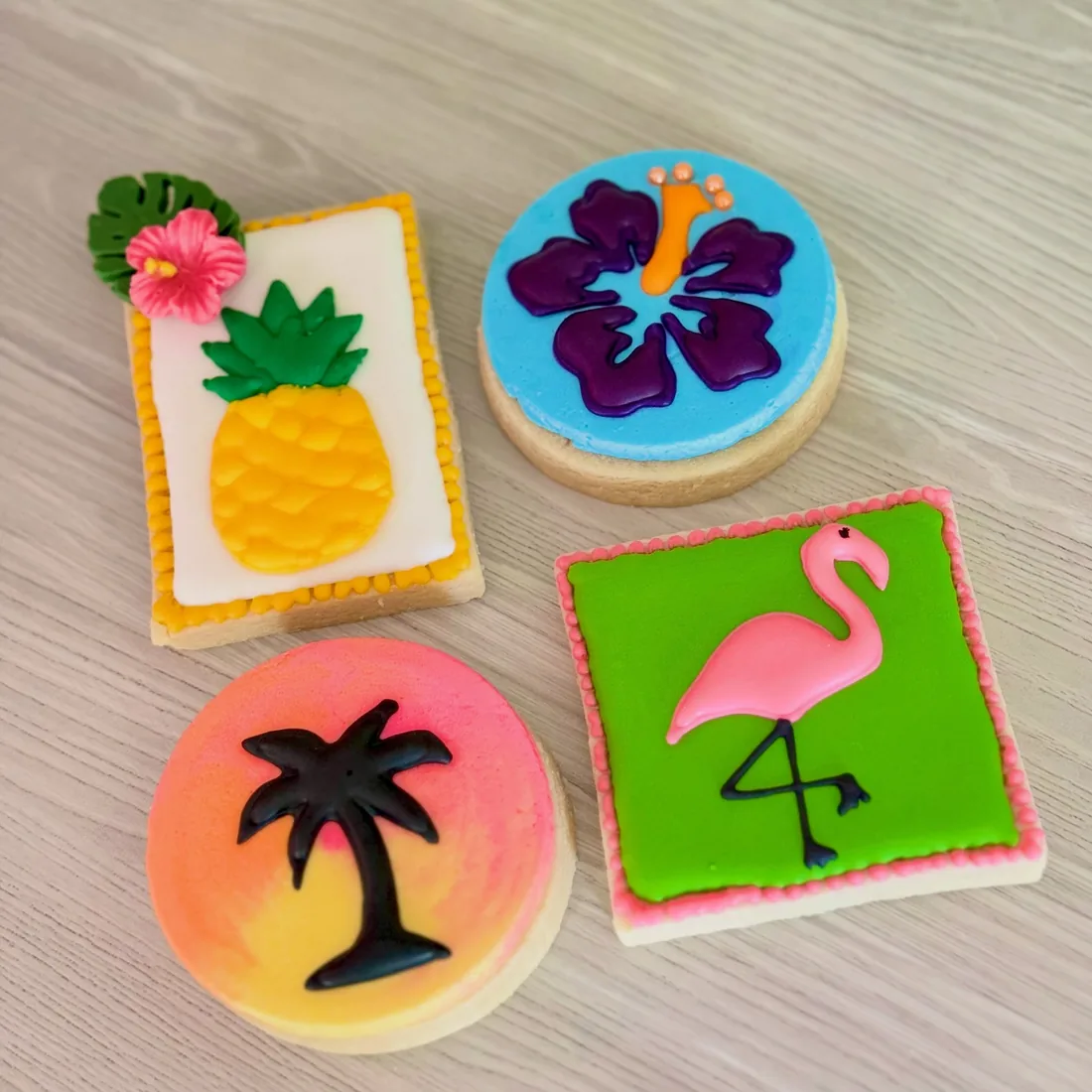 Four tropical cookies: a pineapple, a purple hibiscus, a sunset palm and a pink flamingo