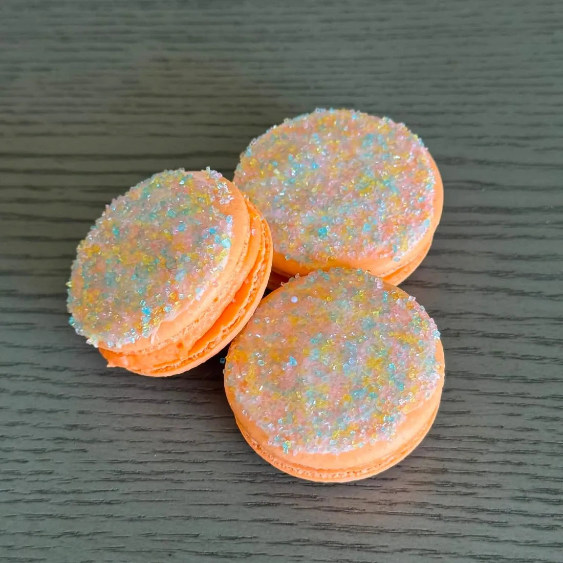 Three peach macarons coated in iridescent pastel sugar crystals