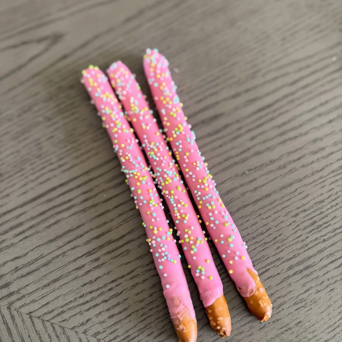 Three pretzel rods dipped in pink white chocolate and covered in pastel sprinkles